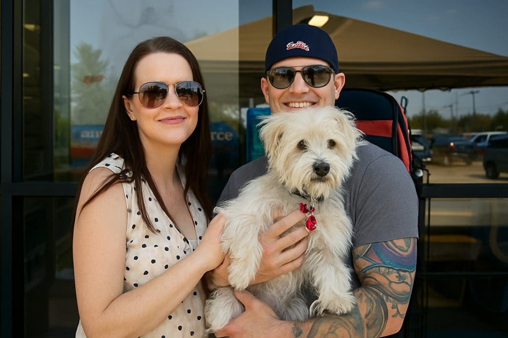 Adoptive couple smiling and holding their fluffy white rescue dog outside a pet store.