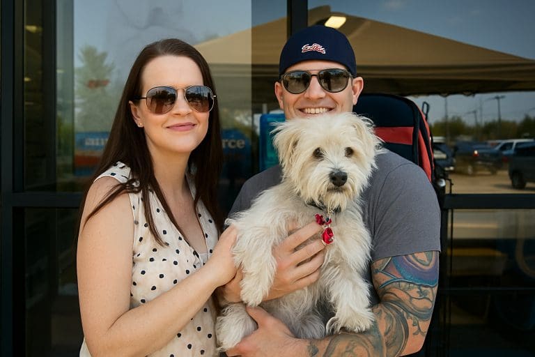 Adoptive couple smiling and holding their fluffy white rescue dog outside a pet store.