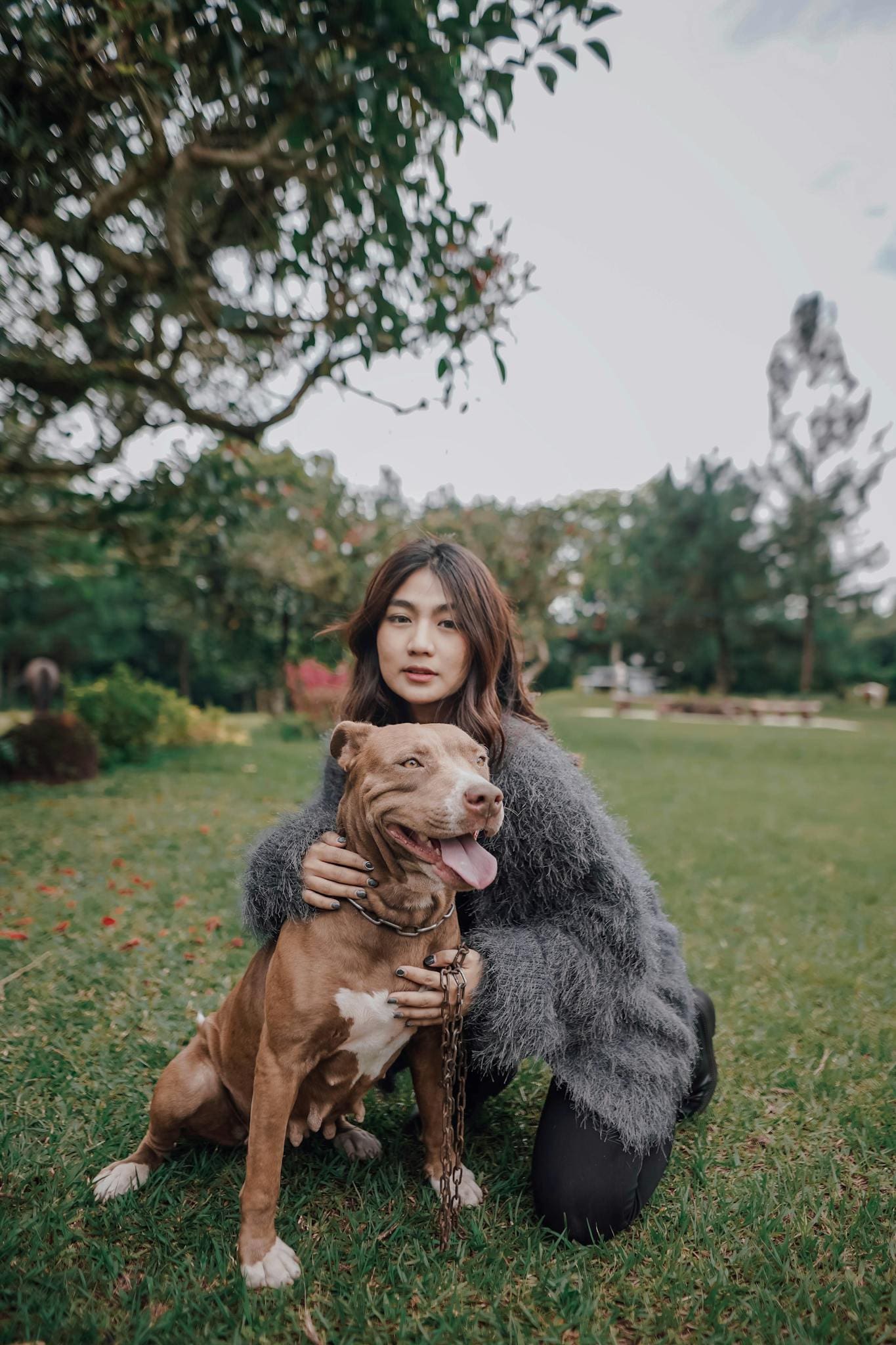 A woman lovingly embraces her dog in a beautiful park setting in Indonesia.
