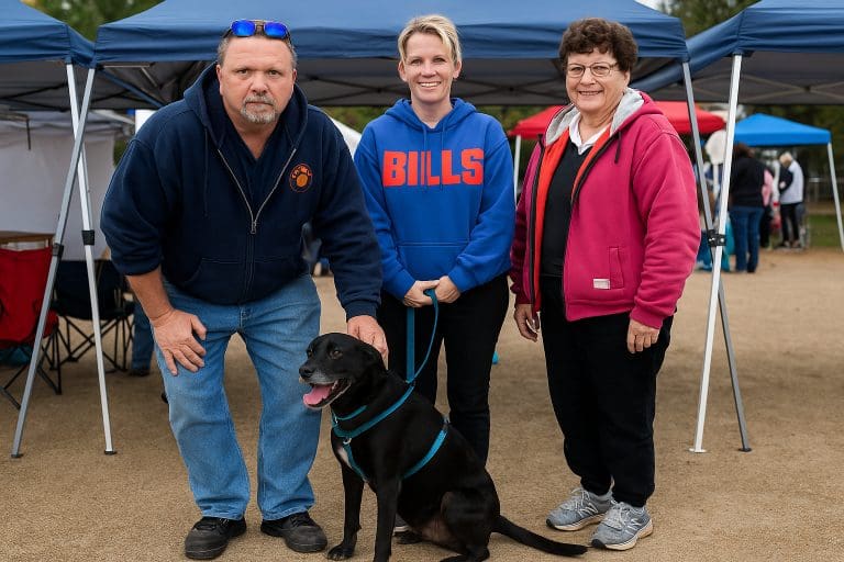 Fergus, a black lab mix, sits happily with his adoptive family at an outdoor reunion event.